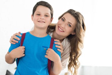 Anne ve küçük çocuk evde, sırt çantası ile geri okul kavramı gülümseyen portresi