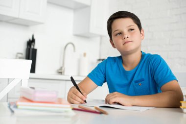 portrait of pensive boy doing homework alone at table at home clipart