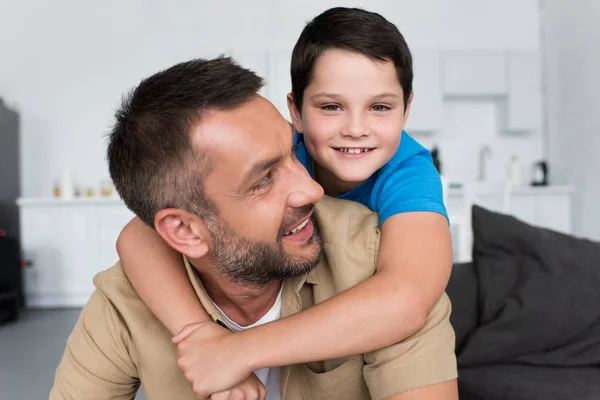 Retrato Menino Sorridente Abraçando Pai Olhando Para Câmera Casa — Fotografia de Stock