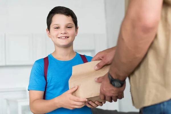 Частковий Вид Батька Дає Паперовий Пакет Їжею Усміхненому Синові Рюкзаком — стокове фото