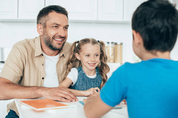 smiling father and kids doing homework together at home