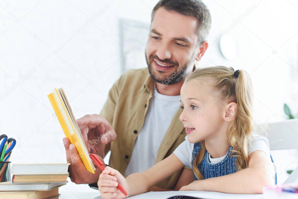 smiling father and little daughter doing homework together at home