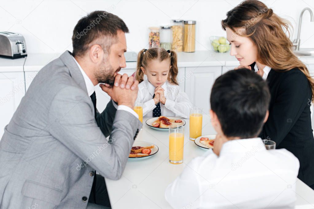 family praying at table during breakfast in kitchen at home