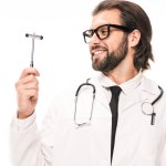 Smiling doctor in white coat and eyeglasses holding reflex hammer isolated on white