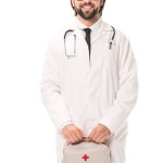 Medico in occhiali che tiene kit di pronto soccorso e sorride alla telecamera isolata su bianco