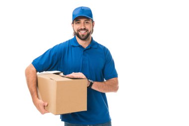 handsome young delivery man holding cardboard box and smiling at camera isolated on white clipart