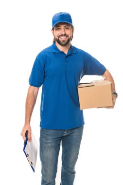smiling young delivery man holding cardboard box and blank clipboard isolated on white 