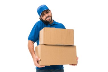 handsome young delivery man holding boxes, talking by smartphone and smiling at camera isolated on white clipart