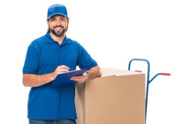happy young delivery man writing on clipboard and smiling at camera isolated on white 