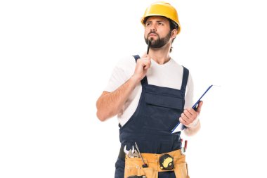 pensive construction worker with tool belt holding clipboard and looking away isolated on white clipart