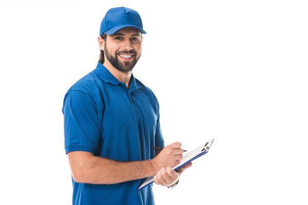 happy young delivery man writing on clipboard and smiling at camera isolated on white