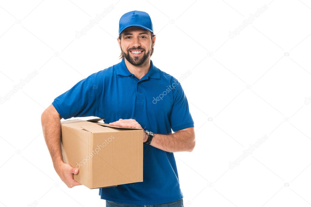 handsome young delivery man holding cardboard box and smiling at camera isolated on white