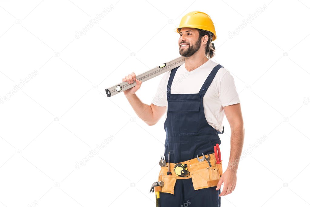 happy handsome workman holding level tool and looking away isolated on white