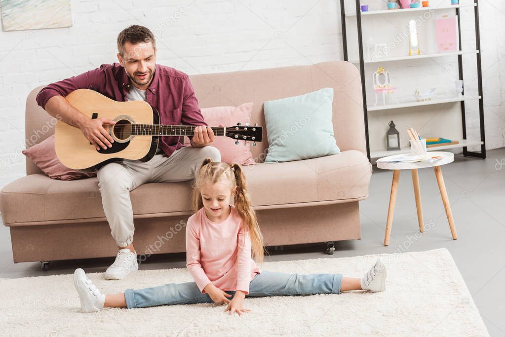 heerful dad playing on guitar while daughter doing split on floor