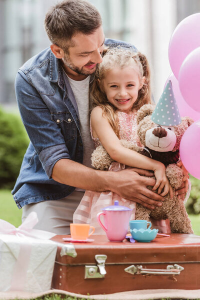 father and daughter with teddy bear playing tea party at lawn