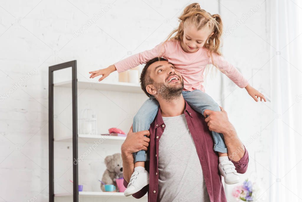 daughter sitting on fathers back and having fun at home