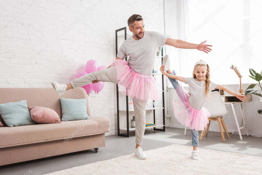 front view of father and daughter in tutu skirts standing on one leg