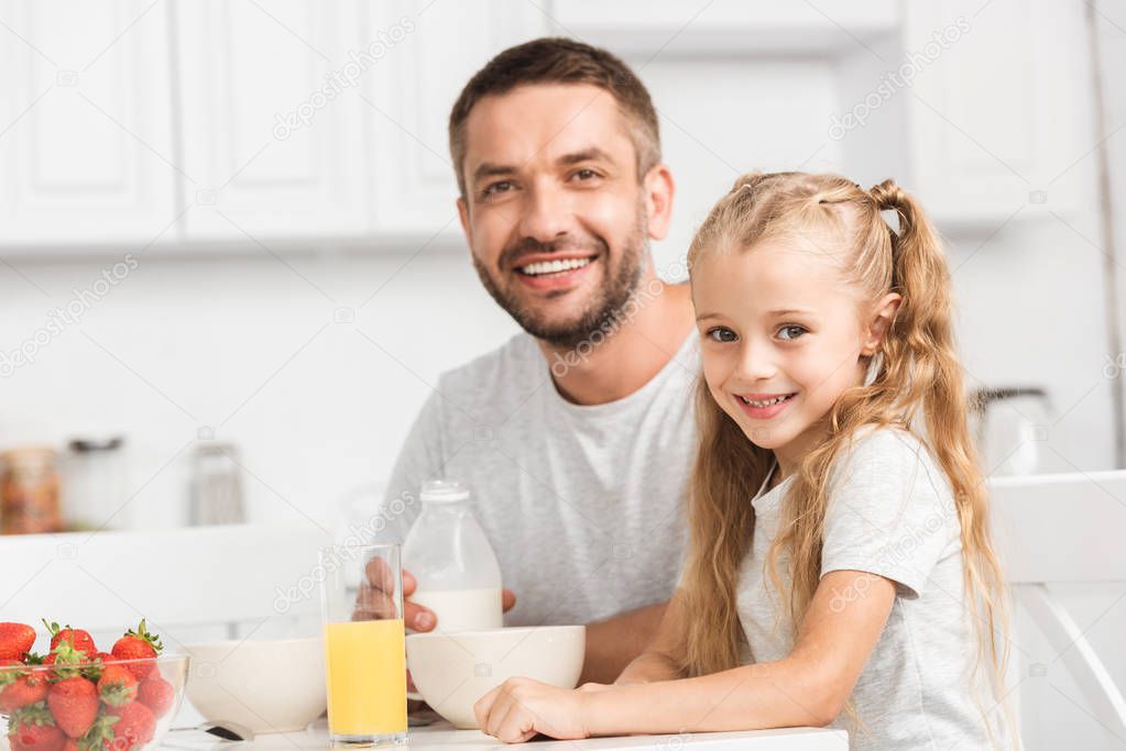 father and daughter having breakfast and looking at camera