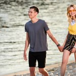 Young couple holding hands and walking on river beach in evening