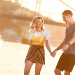 Smiling young couple holding hands and having fun on river beach during beautiful sunset