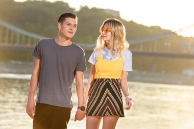 Elele ve günbatımı sırasında nehir kenarında yürüyüş genç çift