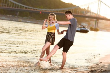 Elele ve nehirde günbatımı sırasında oynayan genç çift