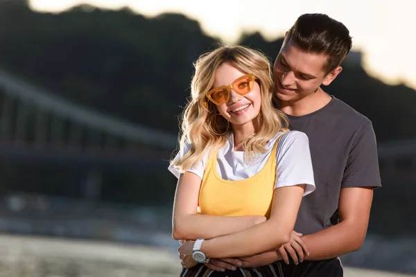 Fidanzato Abbracciare Sorridente Fidanzata Sulla Spiaggia Del Fiume Serata — Foto stock gratuita