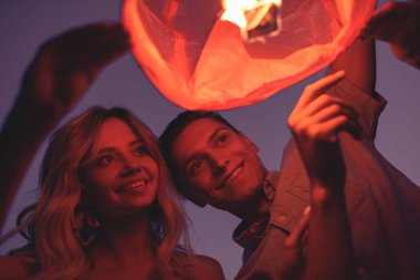 friends launching sky lantern on river beach in evening clipart