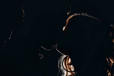 side view of silhouettes of heterosexual couple kissing in dark clipart
