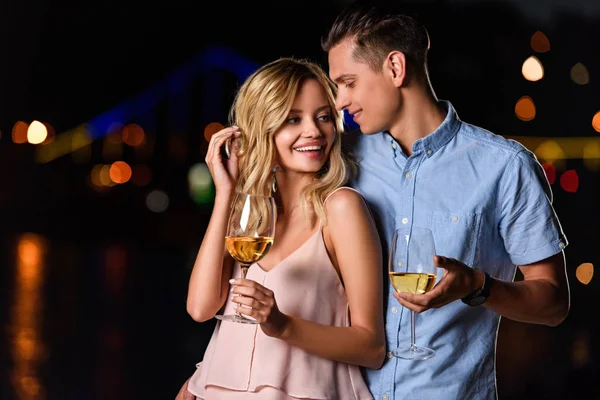 快乐的年轻夫妇站在晚上在河边的白葡萄酒酒杯 — 图库照片
