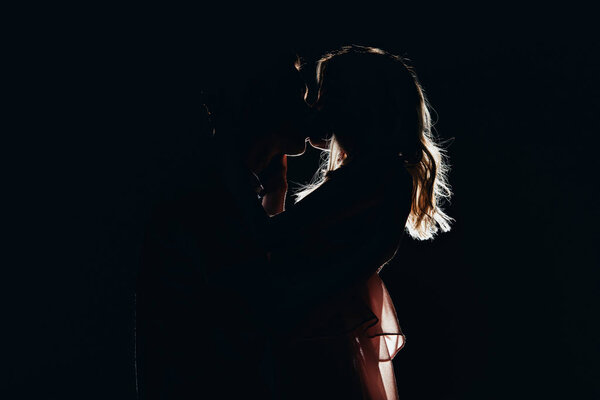 silhouettes of passionate couple kissing in dark
