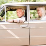 Vista lateral de la sonriente pareja de ancianos sentados en un coche vintage beige