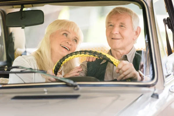 smiling senior wife looking at husband driving retro car