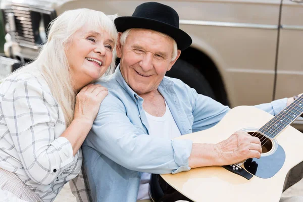 Schöne Seniorin Umarmt Mann Der Gitarre Gegen Beigen Oldtimer Spielt — kostenloses Stockfoto