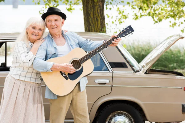 Attractive Senior Woman Embracing Man Playing Guitar Beige Vintage Car — Free Stock Photo