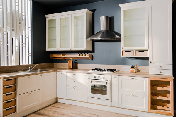 interior of modern light kitchen with white wooden kitchen counters, shelves and stove