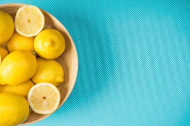 Top view of yellow lemons in wooden plate on turquoise background with copy space clipart
