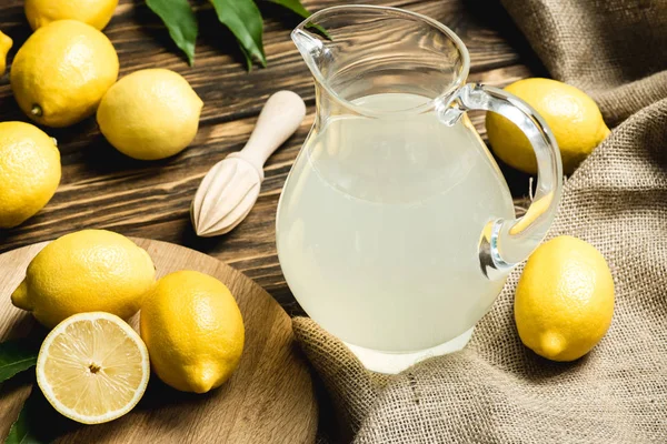 Glass Jug Fresh Juice Squeezer Yellow Lemons Sacking Wooden Surface — Stock Photo, Image