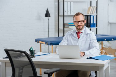 Hastane içinde laptop ile işyerinde beyaz montlu erkek masör gülümseyen portresi