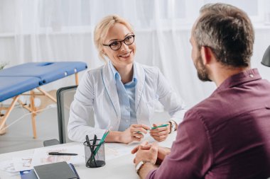 fizyoterapist beyaz ceket Kliniği randevu sırasında hastaya bakarak gülen