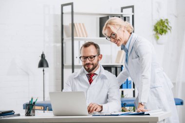 Fizyoterapistler beyaz kat laptop birlikte klinikte kullanılması olarak gülümseyen 