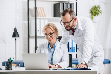 Fizyoterapistler beyaz kat laptop birlikte klinikte kullanılması olarak gülümseyen 