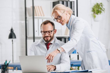 Fizyoterapistler beyaz kat laptop birlikte klinikte kullanılması olarak gülümseyen 