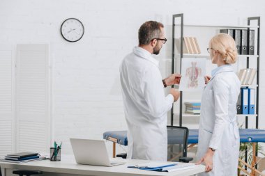 arkadan görünüşü Fizyoterapistler beyaz ceket ve klinik çalışmalarında tartışırken gözlük 