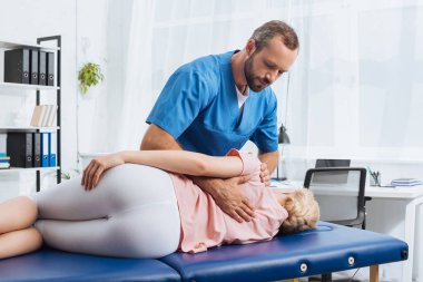 chiropractor massaging back of patient that lying on massage table in hospital clipart