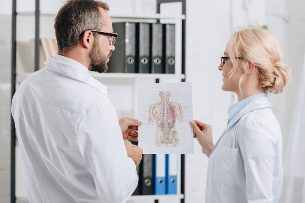 назад взгляд физиотерапевтов в белых халатах и очках, обсуждающих работу в клинике
 