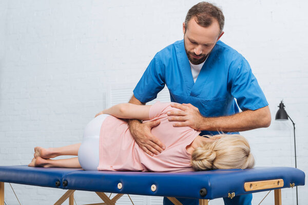 портрет мануального терапевта, массирующего спину пациенту, лежащему на массажном столе в больнице
