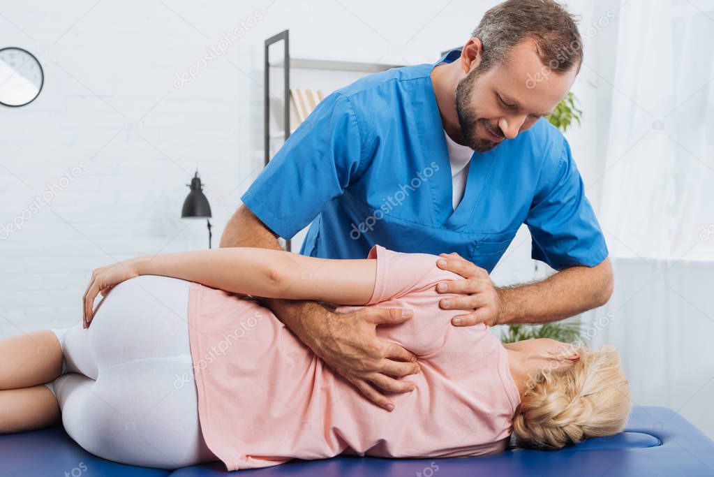 portrait of smiling chiropractor massaging back of patient that lying on massage table in hospital