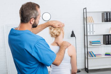 chiropractor stretching neck of woman during appointment in hospital clipart