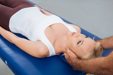 partial view of physiotherapist massaging neck of patient that lying on massage table in clinic clipart